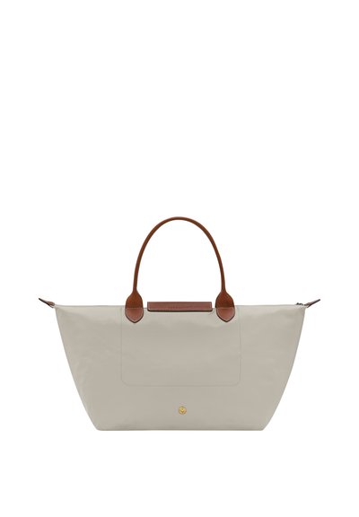 Beige tote bag with wide base, brown leather handles, and a small gold button detail on the front, against a white background.
