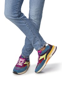 Zapatillas coloridas que combinan detalles en azul, morado, amarillo y naranja. El material mezcla malla y ante con una suela gruesa y con patrón.