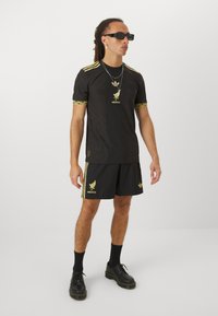 Fekete sportos öltözet, textúrált felső arany díszítéssel, Mexikó logóval, és hozzáillő rövidnadrág három csíkkal és logóval.