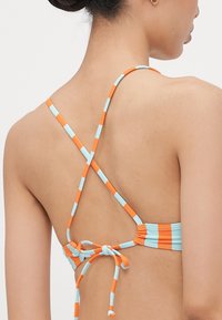 Striped bikini top featuring blue and orange colors, with adjustable crisscross straps and a tied back design. Smooth texture throughout.
