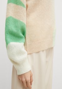 Lekki sweter dziany w kolorze brzoskwiniowym z kolorowymi blokami w odcieniach zieleni i bieli na rękawach, o miękkiej fakturze i prążkowanych mankietach.