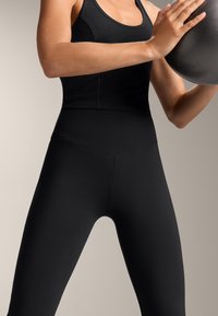 Leggings atletice negre, fabricate dintr-un material elastic, cu o textură netedă, talie înaltă și un design ajustat. Utilizate într-un context de exerciții.