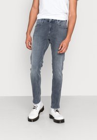 Vaqueros ajustados en gris descolorido, con cinco bolsillos y cierre de botones, combinados con zapatos blancos con cordones y una camiseta blanca lisa.