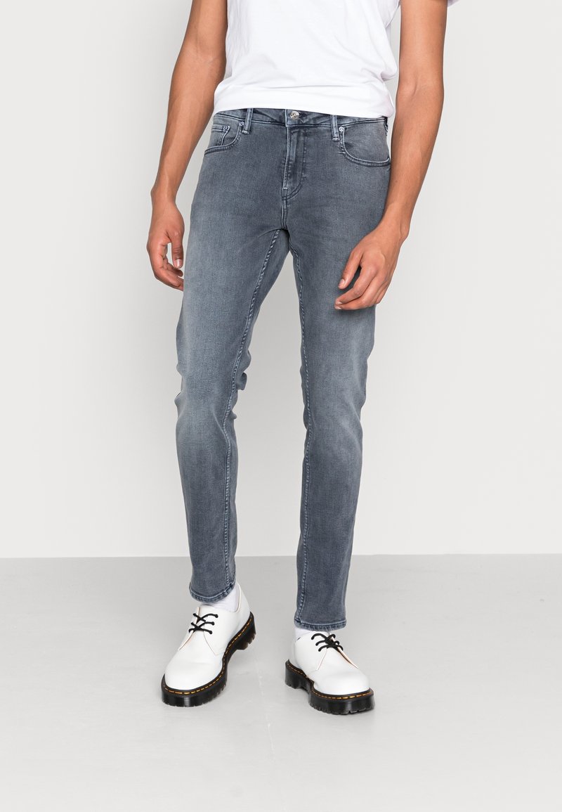 Vaqueros ajustados en gris descolorido, con cinco bolsillos y cierre de botones, combinados con zapatos blancos con cordones y una camiseta blanca lisa.