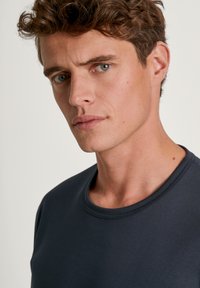 Donkerblauwe crewneck t-shirt met een zachte textuur, met een ribgebreide halslijn. Close-up van het gezicht van een mannelijke model, met minimale details.