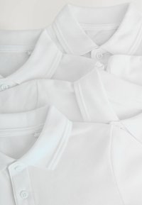 Drei weiße Poloshirts eng übereinander gestapelt, wobei ihre Kragen und Knöpfe hervorgehoben werden, vor einem schlichten Hintergrund.