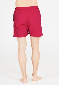 Röda badshorts i lätt material, med elastisk midja och sidofickor. Längden är över knäet med en strukturerad yta.