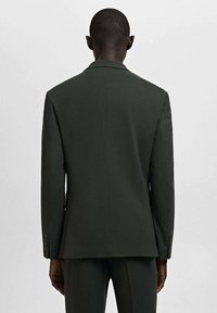 Dunkelgrüner, maßgeschneiderter Blazer mit glatter Textur, einem einzelnen Rückenschlitz und schlankem Schnitt. Verfügt über Knopfakzente an den Ärmeln.