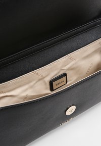 Intérieur d'un sac à main en cuir noir avec doublure en tissu beige, présentant une étiquette de marque en métal et un détail de fermeture magnétique circulaire.