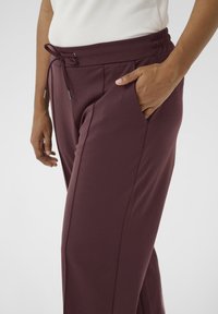 Burgundy elastic waistband pants with a drawstring, featuring side pockets and a smooth texture, tapered design, and minimal seam detailing.