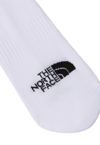 Biela ponožka s rebrovanou textúrou a čiernym logom, ktoré obsahuje nápis "THE NORTH FACE" a zakrivený akcentový dizajn blízko päty.