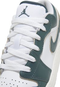 Hvid og mørkegrøn lædersneaker med hvide snørebånd og et Jumpman-logo på tungen, vist i nærbillede fra top.