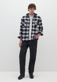 Schwarz-weiße karierte Flanellhemd mit zwei Brusttaschen, über einem weißen T-Shirt geschichtet, kombiniert mit dunklen Jeans und schwarzen Stiefeln.