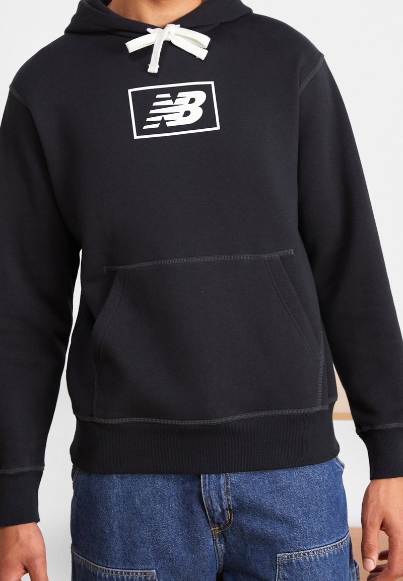 Black hooded sweatshirt made of soft fabric features a front pocket, white logo on chest, and contrasting drawstring. Minimalist design.