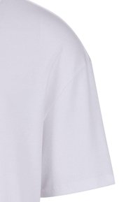 Tricou alb din bumbac, arătând un prim-plan al mânecii și umerilor. Are o textură ribbed și un design drept.