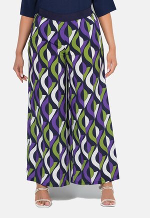 Weite Hosen in Marineblau mit einem geometrischen Muster in Lila, Grün und Weiß. Elastischer Bund und leichter Stoff. Sandalen mit silbernen Riemen.