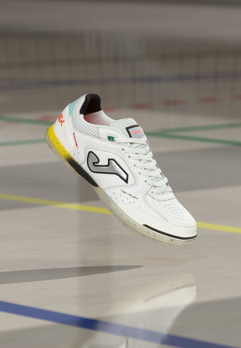 Biały but sportowy ze skóry perforowanej z czarnymi akcentami. Posiada wielokolorową podeszwę i wyraźne logo po boku. Szczegóły z wyraźnym przeszyciem.