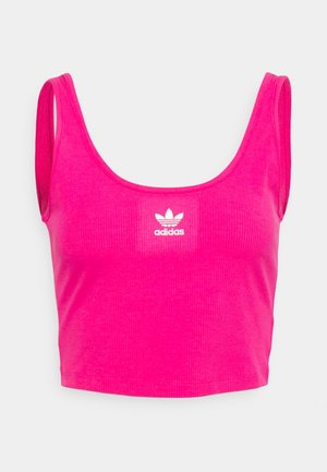 Jasnoróżowy krótki top na szerokich ramiączkach z białym logo Adidas na środku klatki piersiowej na jednolitym jasnym tle.