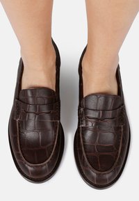 Brown leather loafers with a crocodile texture, featuring a raised seam and a slightly rounded toe. Flat soles and no visible hardware.