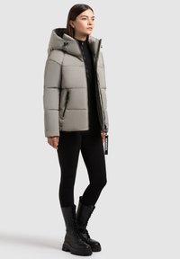 Puffet lys grå jakke med hætte, to sidelukninger og en holdbar tekstur, parret med sorte ribbede leggings og sorte snørebåndsstøvler.