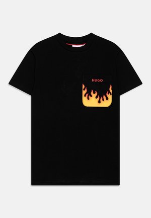 T-shirt noir à manches courtes avec une poche poitrine présentant un design de flammes jaunes et oranges et un texte rouge "HUGO" au-dessus des flammes.