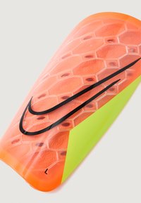 Espinillera de Nike en un brillante color naranja con textura hexagonal, que presenta un logo de swoosh negro y un acento verde en un lado.