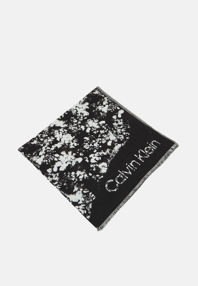 Écharpe noire et blanche avec motif abstrait éclaboussé et logo "Calvin Klein" le long d'un bord, avec des extrémités à franges.