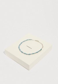 Pulsera de piedra preciosa azul con detalles en plata, que presenta varias piedras talladas dispuestas en un patrón delicado, exhibida sobre una caja blanca.