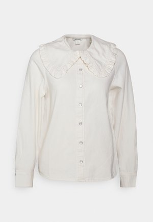 Camisa blanca de manga larga con botones a presión en el frente y gran cuello con volantes.