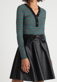 Striped long-sleeve top in teal, black, and white, features a V-neck and three black buttons; paired with a high-waisted black faux leather skirt.