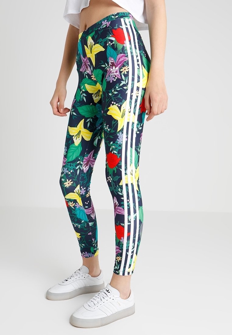 Floral leggings in dark blue featuring colorful lily and rose patterns, finished with three white side stripes. Paired with white sneakers.