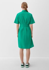 Sukienka z krótkim rękawem i kołnierzykiem w jaskrawym zielonym kolorze, z dopasowanym wcięciem w talii i luźną, średniej długości spódnicą. Noszona z codziennymi trampkami.