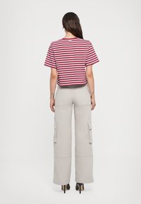 Bordeauxrood en witte gestreepte cropped t-shirt, gecombineerd met beige cargobroek met zijzakken, rustend op hakken, gezien van achteren.