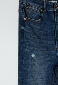 Blue denim jeans featuring a distressed area on the front, copper-tone hardware, standard five-pocket design, and textured fabric.