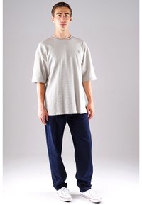 Hellgraues, übergroßes T-Shirt mit kurzen Ärmeln und rundem Halsausschnitt, kombiniert mit dunkelblauen, lässig sitzenden Jeans und weißen Turnschuhen.