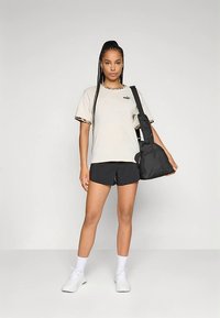 Beeži t-särk leopardimustrilise äärisega, mustad lühikesed püksid, valged sokid ja kingad, hoiab musta õlakotti. Lihtne, vabaaja spordiriietus.