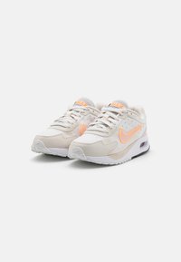 Baskets beiges en matériaux mesh et daim, avec un logo Nike orange, des accents texturés et une unité d'air visible dans la semelle.