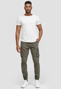 Hvid kortærmet t-shirt parret med olivengrønne cargo-bukser med sidelommer og elastiske manchetter, suppleret med hvide sneakers.