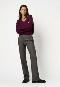 V-neck purple sweater with long sleeves paired with gray flared trousers; model stands with arms crossed, wearing black shoes.