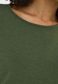 T-shirt in cotone a costine verde scuro con scollatura rotonda. Il tessuto appare morbido con una superficie liscia e un design attillato.