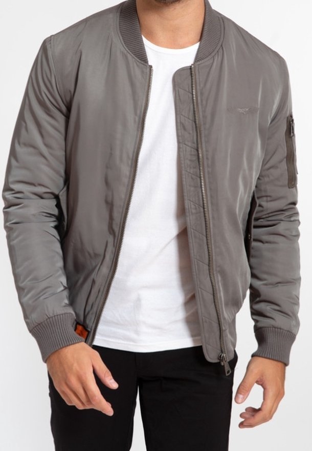 Man wearing unzipped gray bomber jacket over white t-shirt and black pants, standing with arms relaxed at sides.