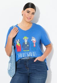 Camiseta azul con un gráfico de tres animales vestidos con ropa colorida, con el texto "SALUT SALUT." Mangas cortas y diseño de cuello en V.