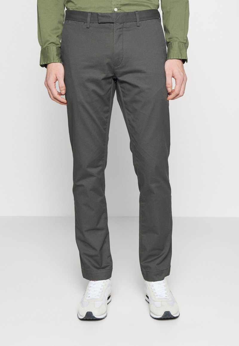 Grå, slim-fit byxor i bomullsmaterial med en slät yta. Har standardfickor, bältesslingor och dragkedja. Kombineras med vita sneakers.