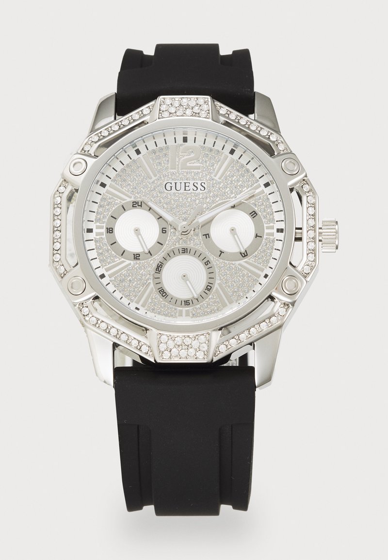 Reloj Guess que presenta una caja octagonal en tono plateado, acentos de cristales brillantes, una esfera plateada con dos subesferas y una correa de silicona negra.
