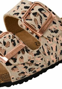 Sandales à glissière imprimé léopard avec une tige en suede beige, des boucles en métal rose gold, et une semelle en caoutchouc noir. Comprend un lit de pied contourné pour plus de confort.