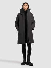 Juodas ilgas paltas su kapišonu, užtrauktuku ir šoninėmis kišenėmis. Modelis dėvi juodas legginsus ir masyvias juodas aulinukes. Lygus, matinės tekstūros audinys.