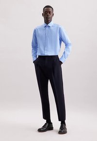Camicia a righe azzurro chiaro con bottoni abbinata a pantaloni scuri su misura e scarpe nere. Caratteristiche includono un colletto appuntito e maniche lunghe.