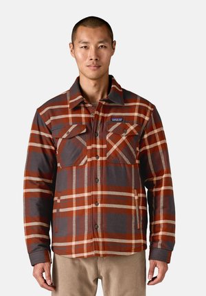 Camicia a quadri con bottoni in arancione, grigio e crema. Presenta due tasche sul petto e colletto. Il tessuto ha un aspetto strutturato.
