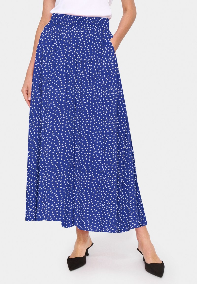 Modrá maxi sukně s bílými puntíky, elastickým pasem, bočními kapsami, splývavou tkaninou a plným siluetu. Stylizováno s černými podpatky.