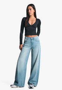 Černý dlouhý rukáv top s výstřihem do V, spárovaný se světle modrými širokými džíny. Džíny mají zesvětlenou úpravu a uzávěr na knoflík.